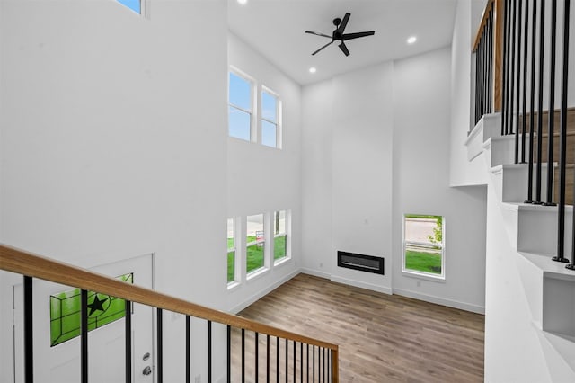 unfurnished living room with light hardwood / wood-style floors, a towering ceiling, and ceiling fan