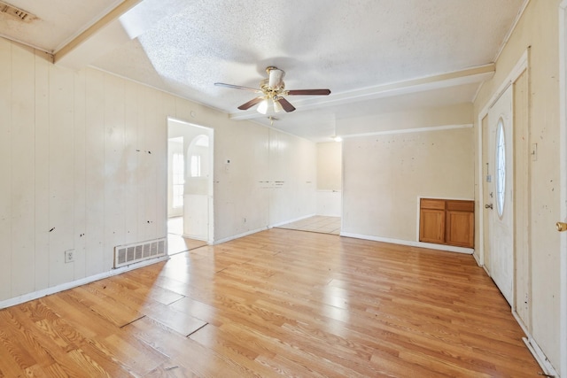 unfurnished room featuring light wood-type flooring, wood walls, ceiling fan, and a textured ceiling