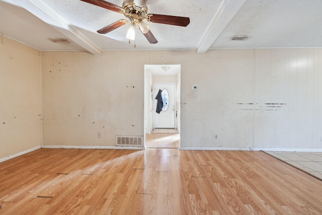 unfurnished room featuring ceiling fan, a textured ceiling, beam ceiling, and light hardwood / wood-style floors