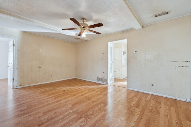 spare room featuring a textured ceiling, ceiling fan, light hardwood / wood-style flooring, wood walls, and beam ceiling