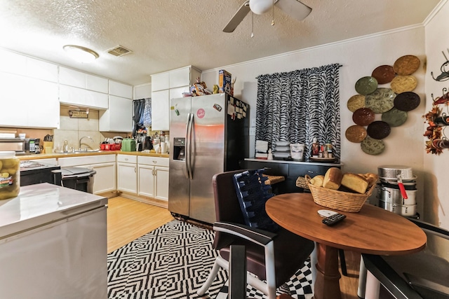 kitchen with stainless steel refrigerator with ice dispenser, ornamental molding, a textured ceiling, sink, and white cabinets