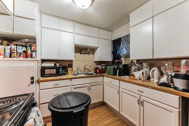 kitchen with sink, light wood-type flooring, a textured ceiling, tasteful backsplash, and white cabinetry