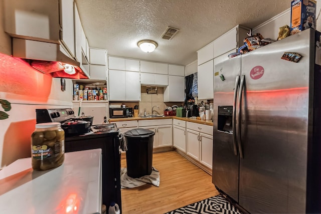 kitchen featuring white cabinetry, sink, stainless steel fridge, light hardwood / wood-style floors, and a textured ceiling