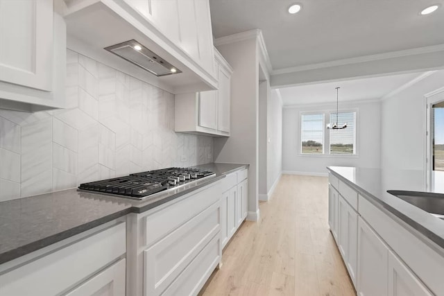 kitchen featuring light wood-type flooring, crown molding, a chandelier, white cabinetry, and stainless steel gas stovetop