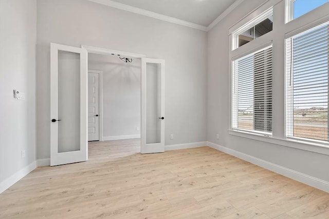 empty room featuring crown molding, french doors, light hardwood / wood-style floors, and plenty of natural light