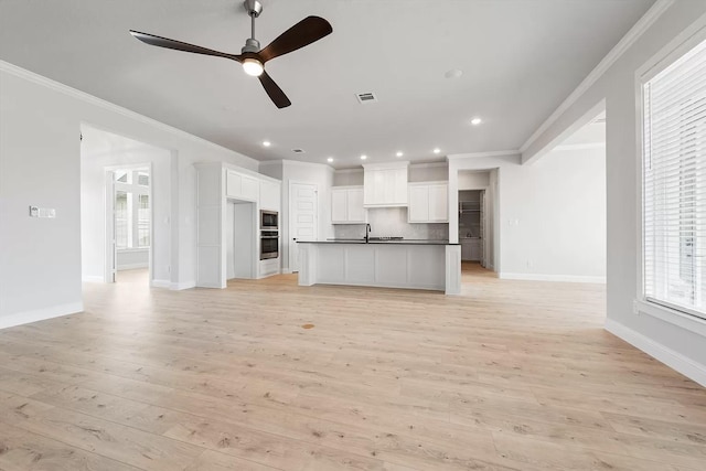 unfurnished living room featuring light hardwood / wood-style floors, ceiling fan, ornamental molding, and sink