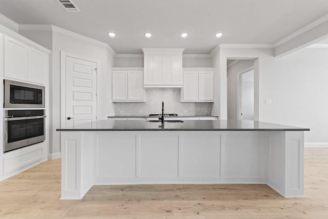 kitchen featuring a center island with sink, oven, and white cabinets