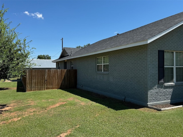 view of side of home with brick siding, a lawn, and a shingled roof