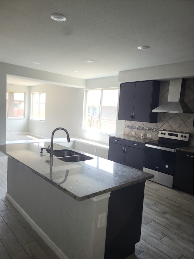 kitchen featuring a center island with sink, electric range, sink, and wall chimney range hood