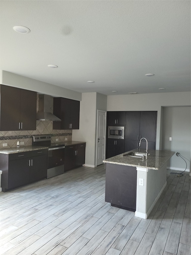 kitchen featuring stainless steel appliances, decorative backsplash, wall chimney exhaust hood, light stone counters, and light hardwood / wood-style floors