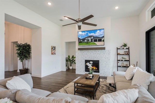 living room featuring a tile fireplace, ceiling fan, dark hardwood / wood-style flooring, and a towering ceiling