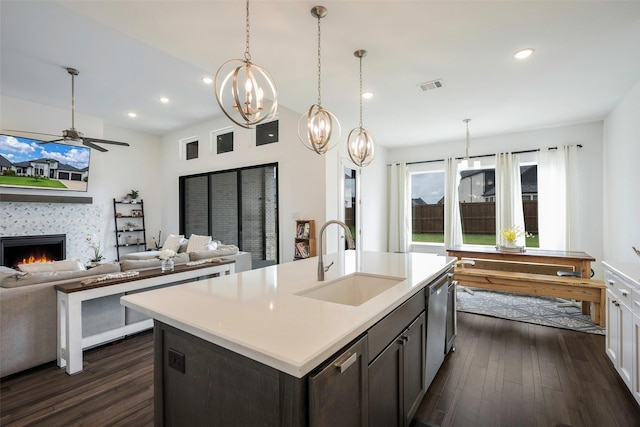 kitchen with dark hardwood / wood-style flooring, sink, an island with sink, and a tiled fireplace