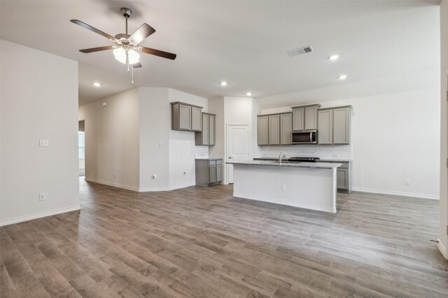 kitchen with light hardwood / wood-style flooring, decorative backsplash, a center island with sink, ceiling fan, and gray cabinets