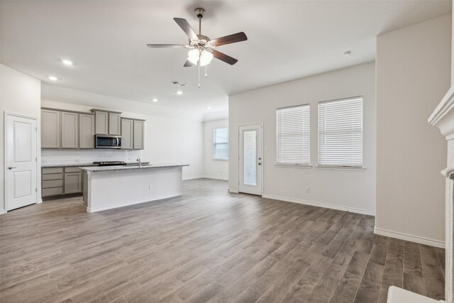 kitchen with hardwood / wood-style flooring, an island with sink, tasteful backsplash, ceiling fan, and gray cabinets