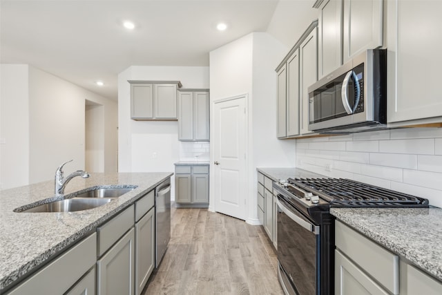 kitchen with backsplash, sink, light wood-type flooring, light stone countertops, and stainless steel appliances