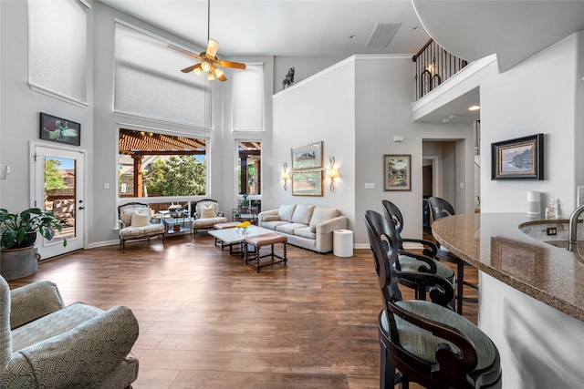 living room with dark wood-type flooring, ceiling fan, and a high ceiling