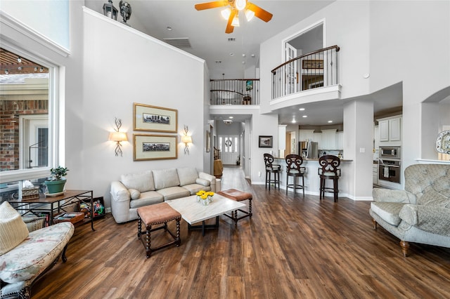 living room with ceiling fan, dark hardwood / wood-style floors, and a towering ceiling