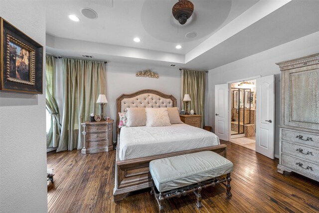 bedroom featuring ceiling fan, ensuite bathroom, dark hardwood / wood-style floors, and a tray ceiling