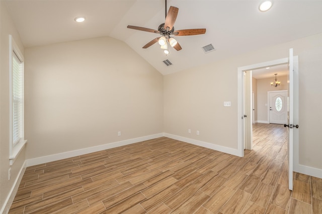 empty room featuring lofted ceiling and ceiling fan with notable chandelier