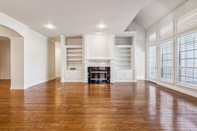 unfurnished living room with ornamental molding, built in shelves, vaulted ceiling, a premium fireplace, and dark hardwood / wood-style floors