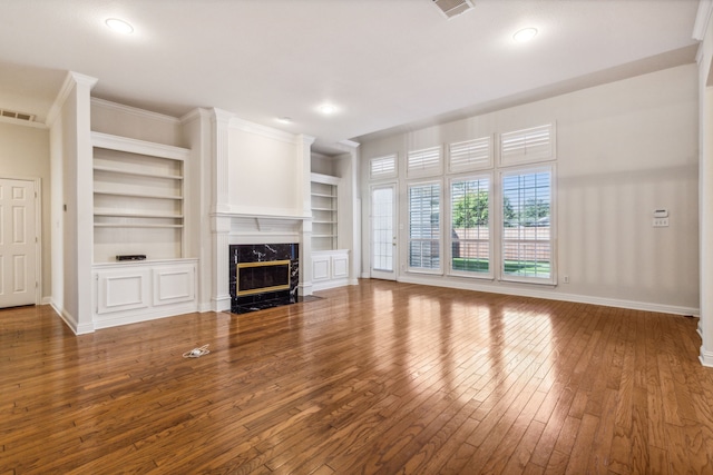 unfurnished living room featuring crown molding, a premium fireplace, built in features, and wood-type flooring