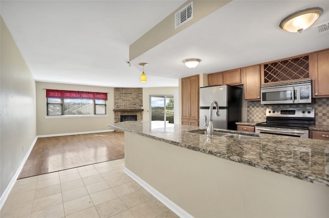 kitchen featuring appliances with stainless steel finishes, dark stone counters, a fireplace, decorative backsplash, and light wood-type flooring