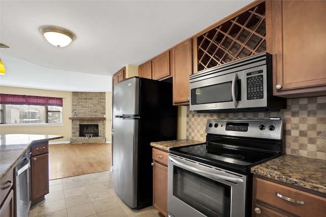 kitchen with tasteful backsplash, light hardwood / wood-style floors, brick wall, appliances with stainless steel finishes, and a fireplace