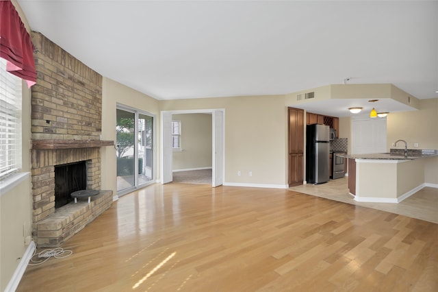 unfurnished living room with a fireplace, sink, light hardwood / wood-style flooring, and brick wall