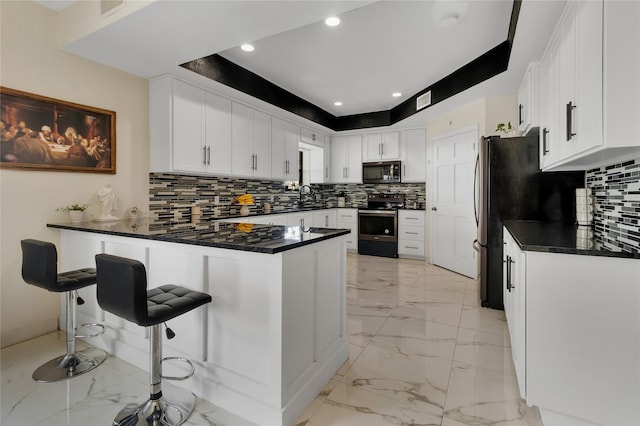 kitchen with kitchen peninsula, a kitchen breakfast bar, stainless steel appliances, sink, and white cabinets