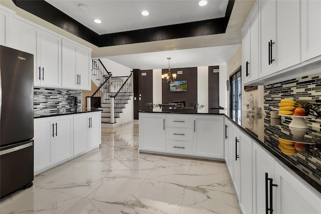 kitchen featuring stainless steel fridge, a tray ceiling, pendant lighting, a notable chandelier, and white cabinetry