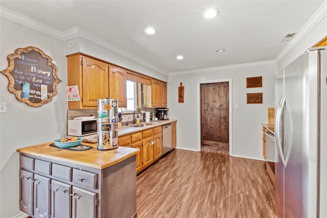 kitchen with crown molding, stainless steel appliances, hardwood / wood-style floors, decorative backsplash, and sink