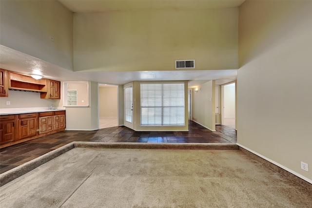 unfurnished living room featuring dark colored carpet and a towering ceiling