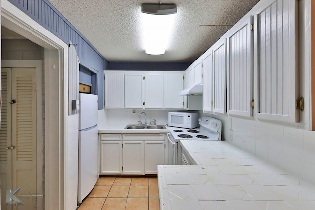 kitchen with light tile patterned floors, white cabinets, a sink, a textured ceiling, and white appliances