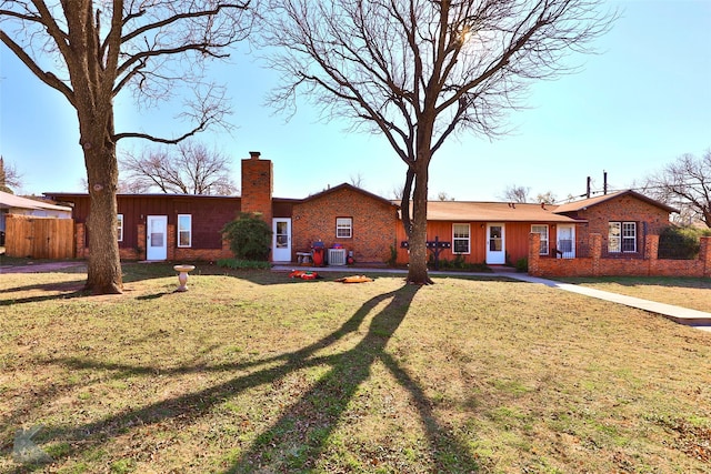 view of front of house with cooling unit, brick siding, fence, a chimney, and a front yard