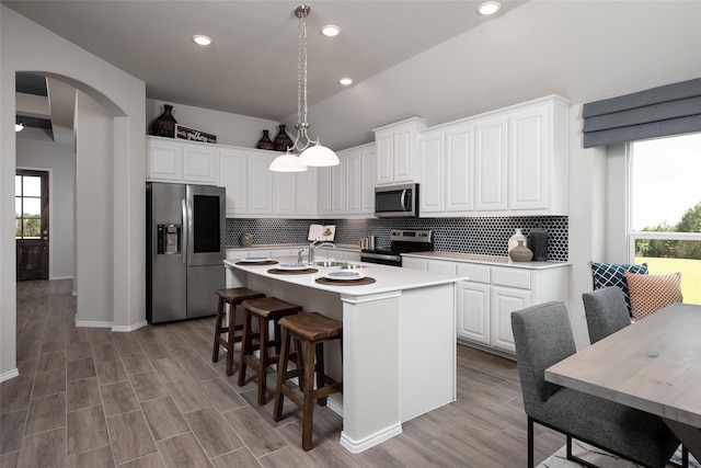 kitchen featuring appliances with stainless steel finishes, tasteful backsplash, white cabinets, decorative light fixtures, and an island with sink