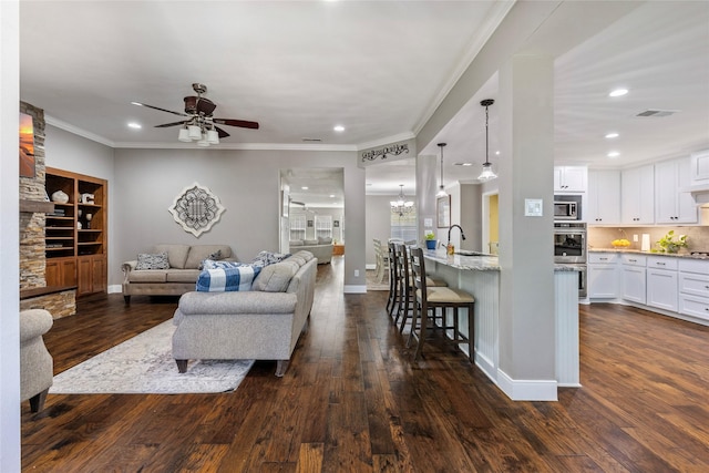 living room with crown molding, ceiling fan with notable chandelier, baseboards, dark wood finished floors, and visible vents