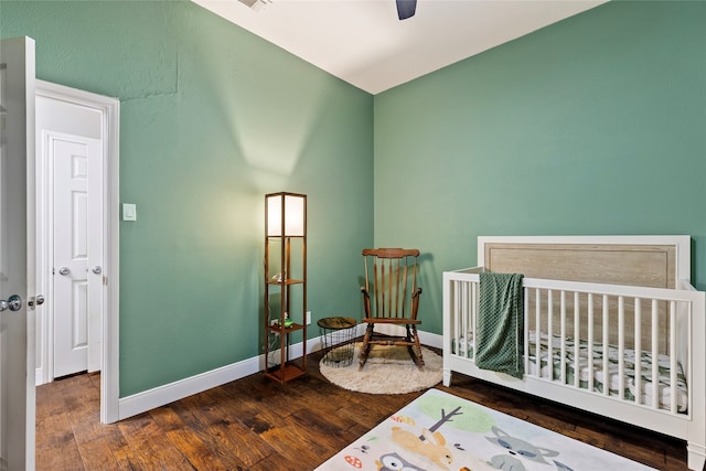 bedroom with a crib, dark hardwood / wood-style flooring, and ceiling fan