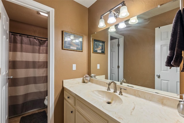 bathroom with a shower with curtain, toilet, vanity, and a textured wall