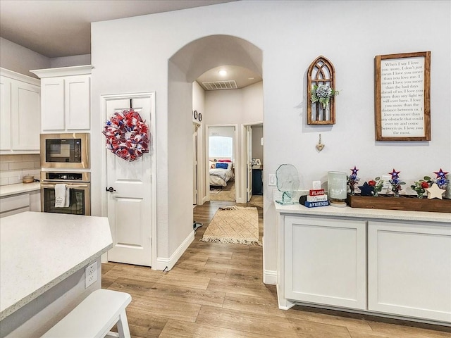 kitchen with decorative backsplash, light wood-type flooring, black microwave, oven, and white cabinetry