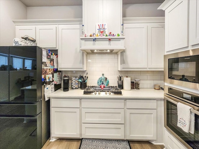 kitchen with decorative backsplash, white cabinets, stainless steel appliances, and light wood-type flooring