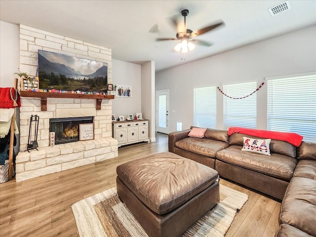 living room with ceiling fan, a stone fireplace, and wood-type flooring