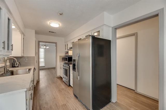 kitchen with appliances with stainless steel finishes, tasteful backsplash, sink, light wood-type flooring, and white cabinetry