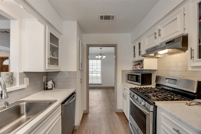 kitchen featuring appliances with stainless steel finishes, light hardwood / wood-style flooring, white cabinets, sink, and backsplash