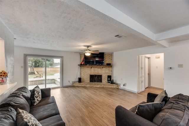 living room with ceiling fan, a textured ceiling, brick wall, light hardwood / wood-style floors, and a brick fireplace