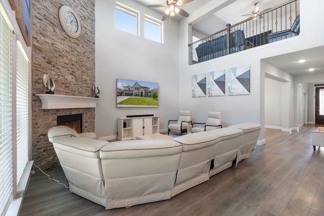 living room featuring a stone fireplace, a towering ceiling, hardwood / wood-style floors, and ceiling fan