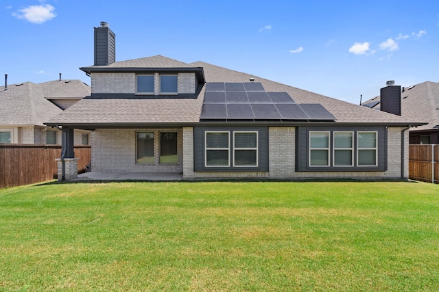 rear view of house featuring solar panels and a lawn