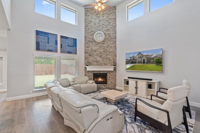 living room with a stone fireplace, ceiling fan, hardwood / wood-style floors, and a towering ceiling