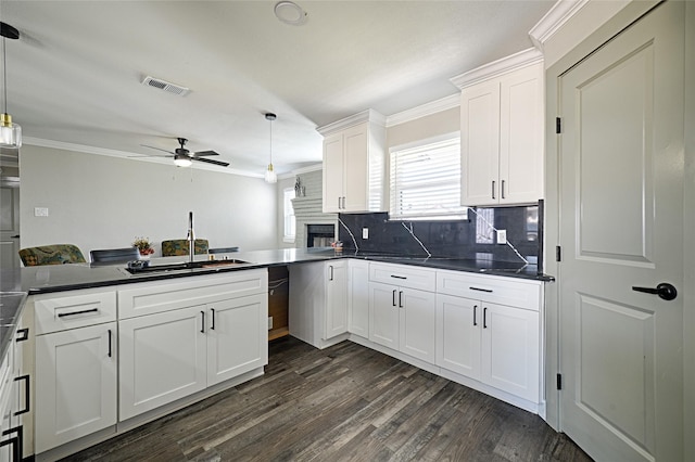 kitchen featuring dark wood finished floors, white cabinets, dark countertops, ornamental molding, and a sink