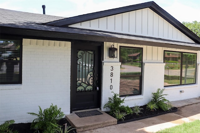 property entrance featuring brick siding, roof with shingles, and board and batten siding