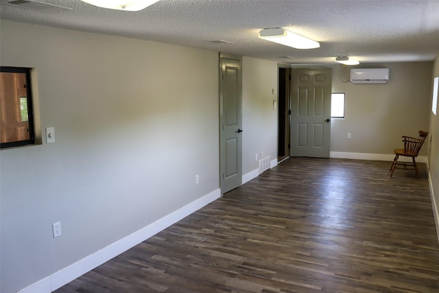 spare room featuring a wall unit AC, baseboards, dark wood finished floors, and a textured ceiling